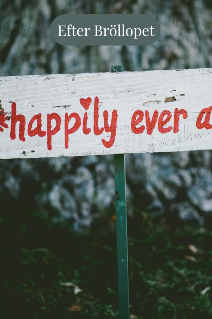 Handmålad skylt med texten “happily ever after” och röd pil, står utomhus mot trädstam – symbol för livet efter bröllopet.